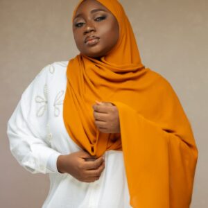 Striking portrait of a woman wearing an orange hijab and white embroidered top.