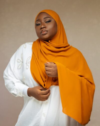 Striking portrait of a woman wearing an orange hijab and white embroidered top.