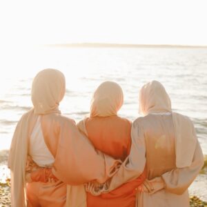 Three women in traditional hijabs enjoying a peaceful sunset on the beach.