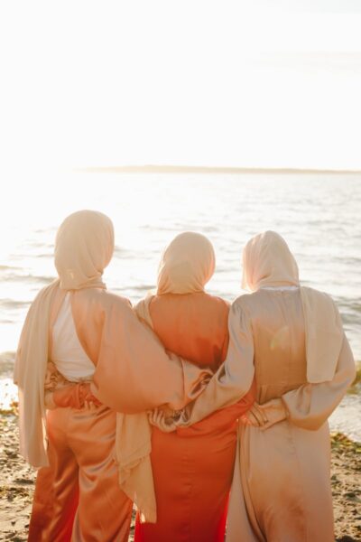 Three women in traditional hijabs enjoying a peaceful sunset on the beach.